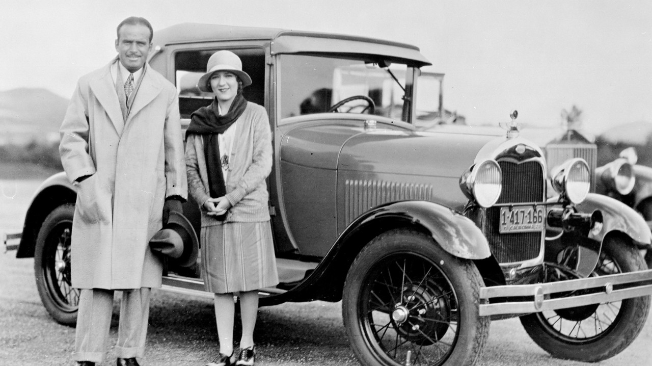 A black and white photo of Doug Fairbanks and Mary Pick with a 1928 Ford Model A Sport Coupe